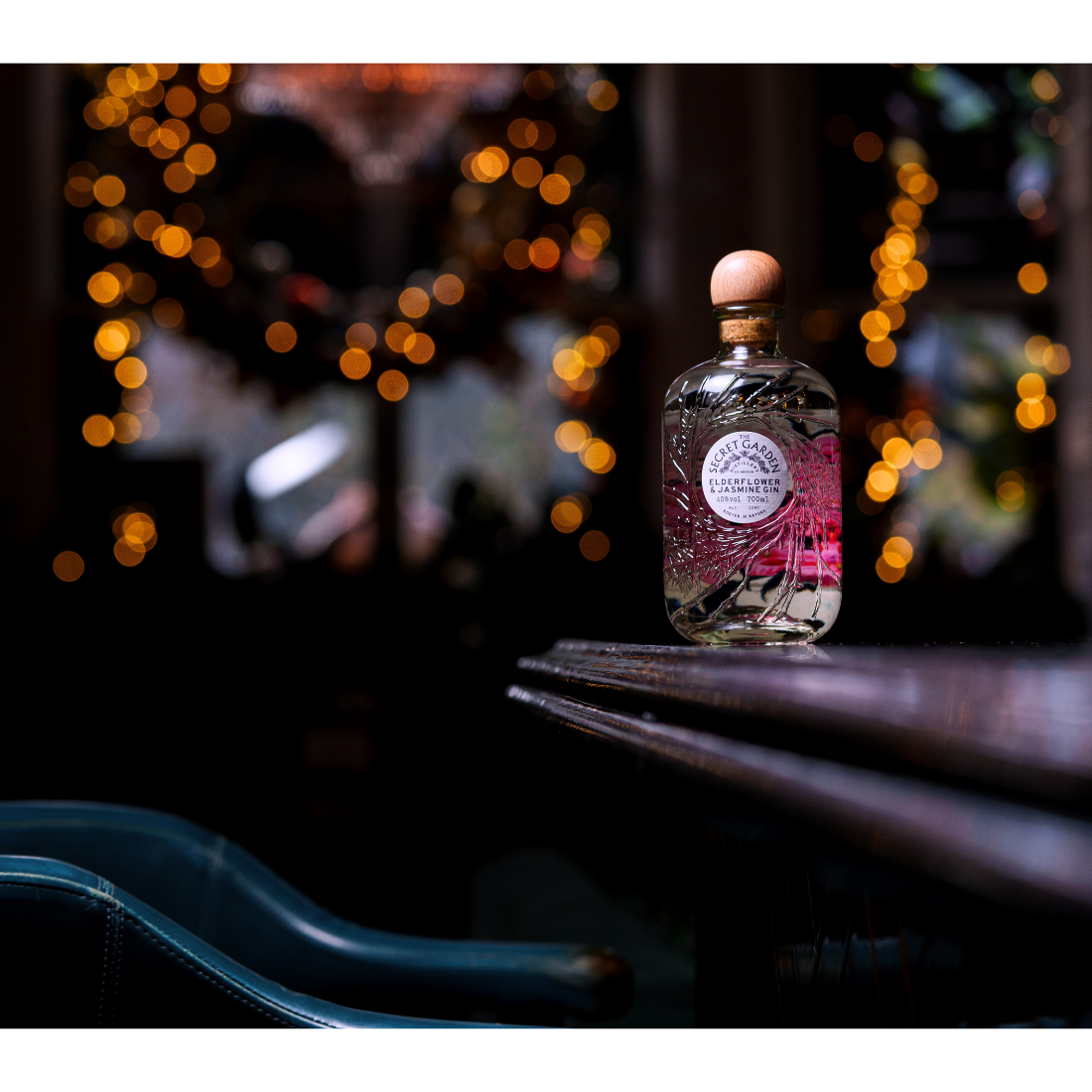 70cl Bottle of Secret Garden pink elderflower & jasmine luxury gin sitting on edge of an Edinburgh bar with festive christmas lights behind